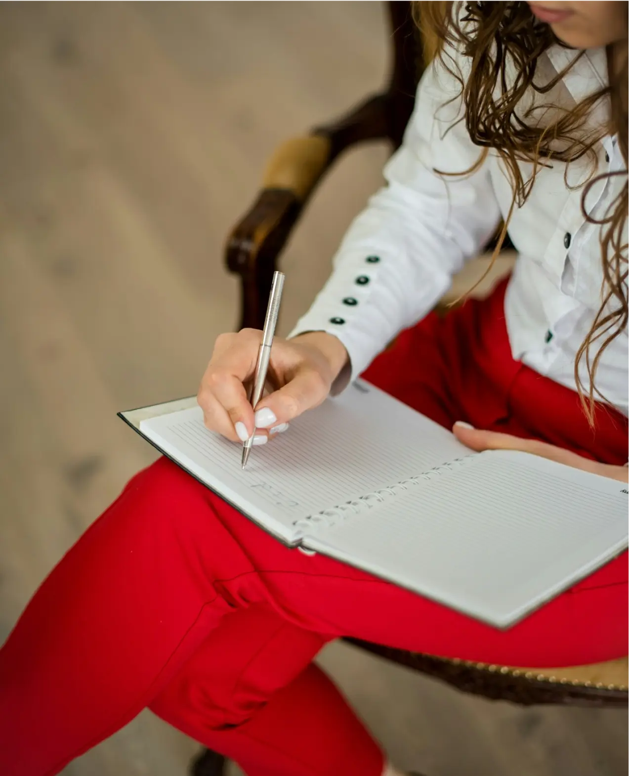 A woman wearing red pants and a white jacket writing in a notebook